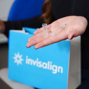 Hand holding a clear Invisalign aligner over branded packaging